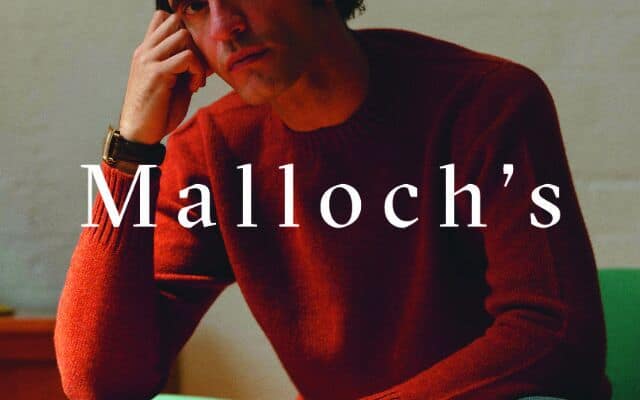 malloch's brand lock up man in british made orange jumper with white logo